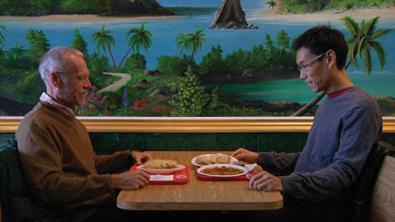 Still depicting two figures sitting across from each other in a booth.