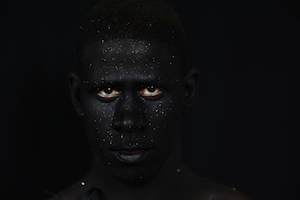Photograph depicting a portrait of a figure with white dots of paint against a black background.
