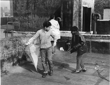 Black and white photograph showing three children playing with a kite.