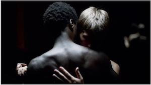 Photograph depicting two figures in an embrace against a black background.