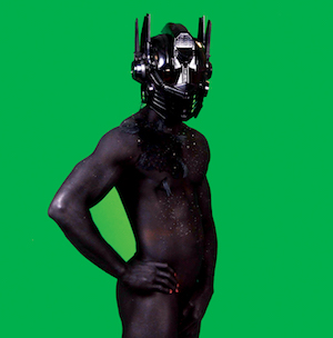 Photograph of a naked figure wearing a mask against a green background.
